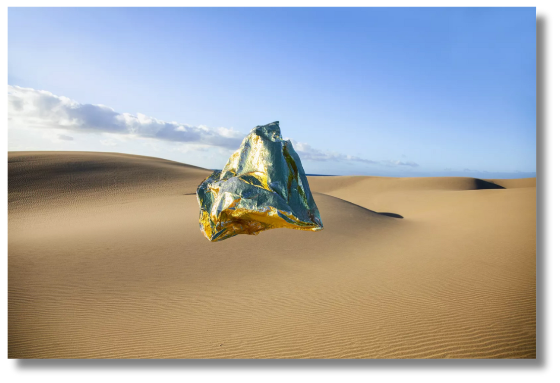 A metallic, gold-and-blue sculptural object floats in the middle of a desert landscape, blending surrealism with environmental contrast.