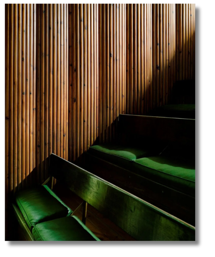 A quiet architectural space with vertical wooden paneling and forest green seating bathed in soft light.