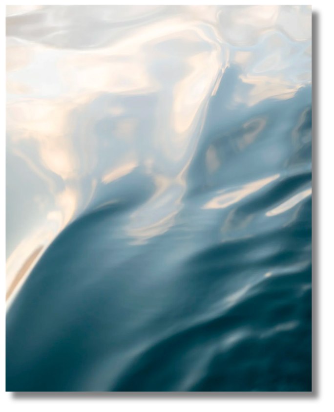a blue, silky photograph of the ocean, the blue flows seamlessly into the white, pearly colored water with sun shining 